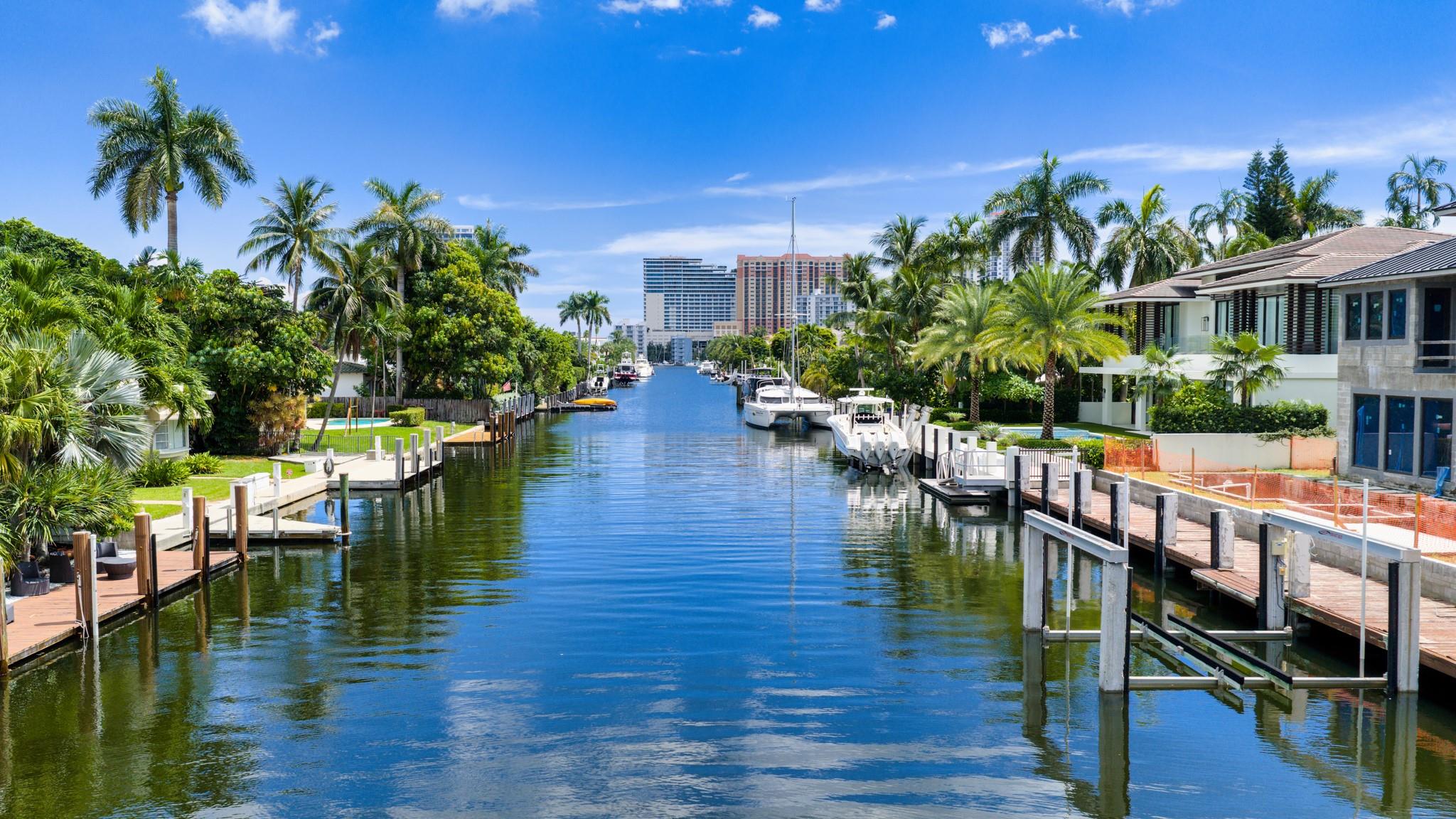 A long canal shot showcasing deep-water dockage and prime waterfront estates set against a backdrop of the oceanfront skyline.