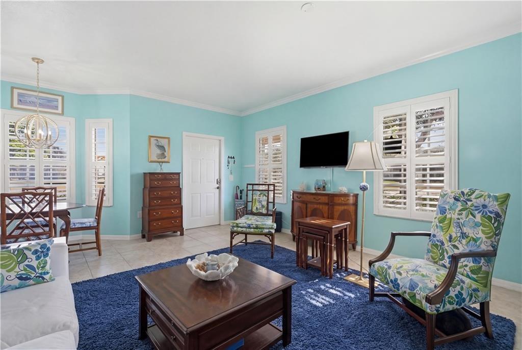 Living room featuring elevated lighting, planation shutters, crown molding, and light tile patterned floors