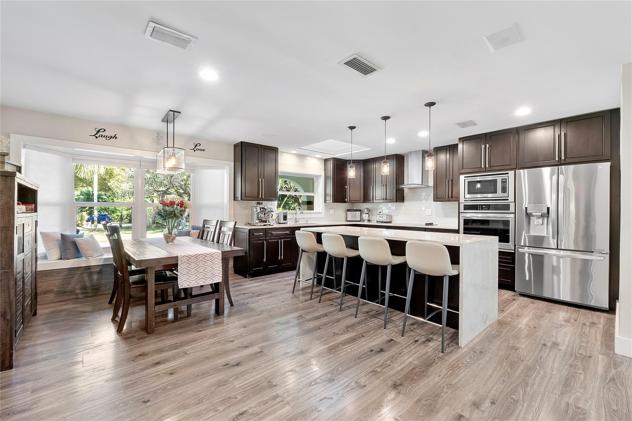 This open floorplan kitchen has premium waterproof wood based laminate flooring, The prettiest bay window with a custom window seat for gazing at nature outside, Lots of space in this area for at least 10 people to casually dine, The kitchen cabinets are custom walnut wood cabinetry and have matching cabinets in the laundry room, LG & Fridgedaire appliances, Double oven/convention & microwave & matching pendant lighting,