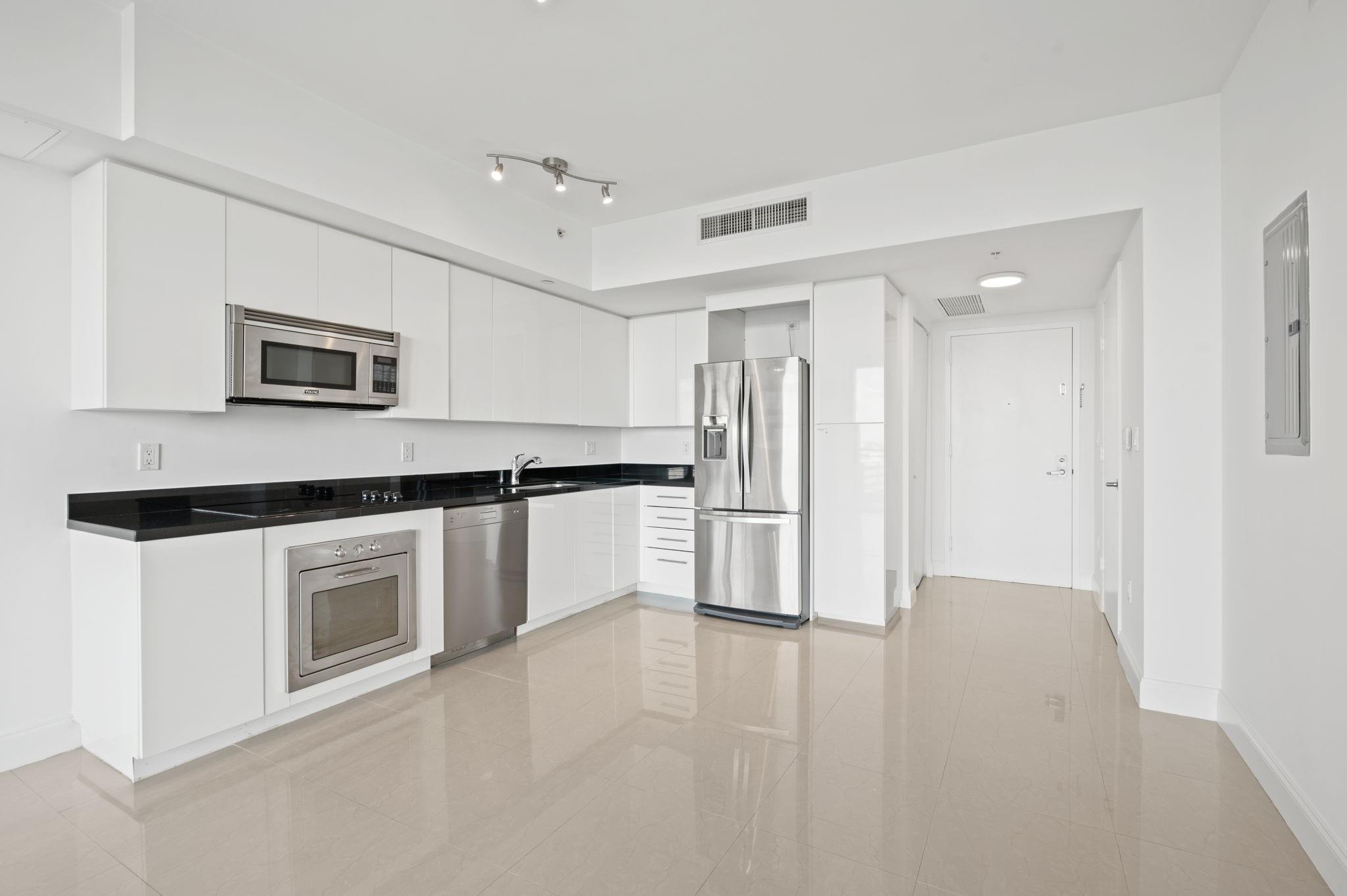 KITCHEN WITH STAINLESS STEEL APPLIANCES, POLISHED BLACK GRANITE COUNTERTOPS AND MODERN WHITE FLAT-PANEL CABINETRY