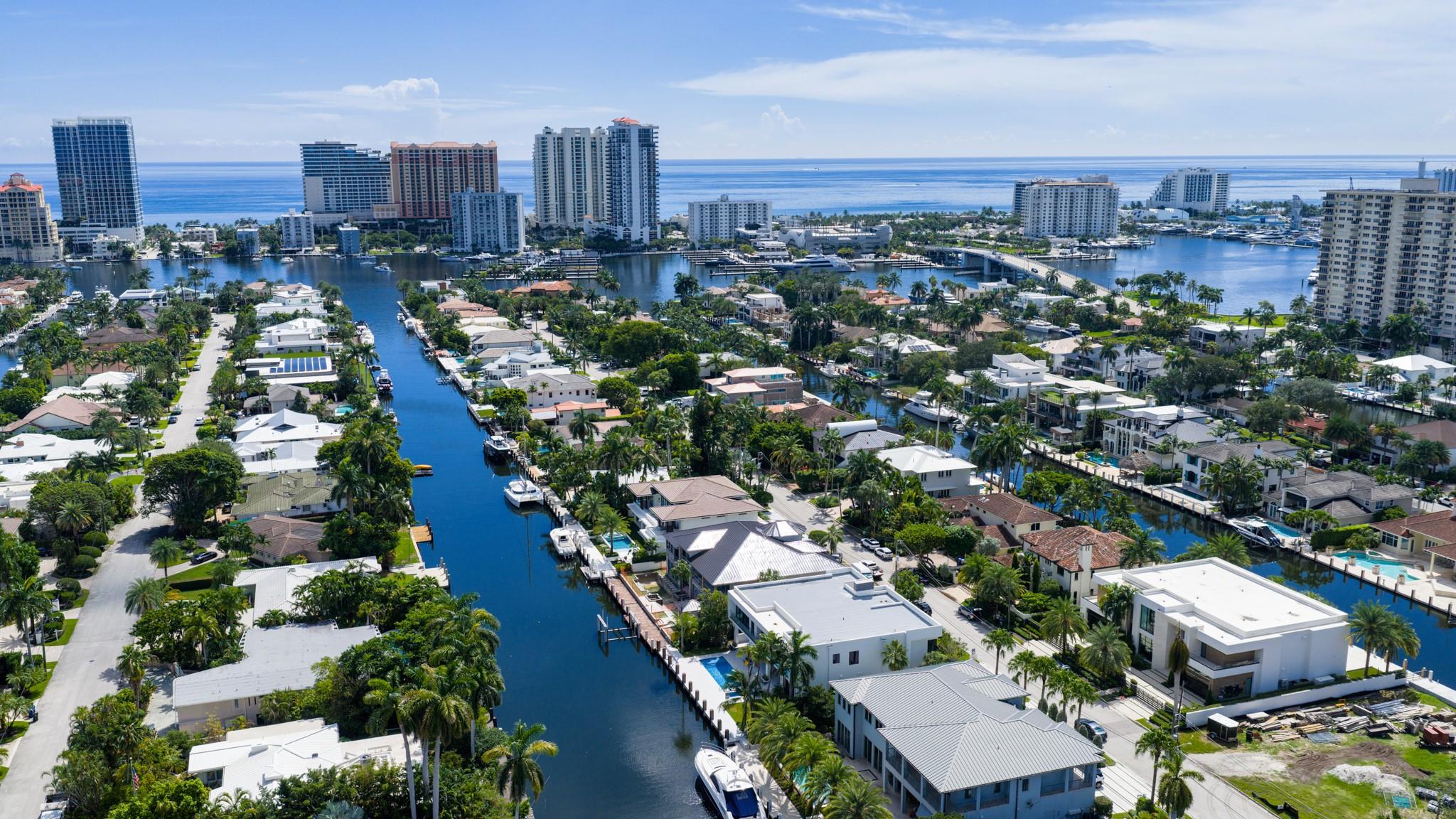 A vibrant neighborhood scene showing waterfront homes leading toward the Fort Lauderdale coastline and ocean horizon.