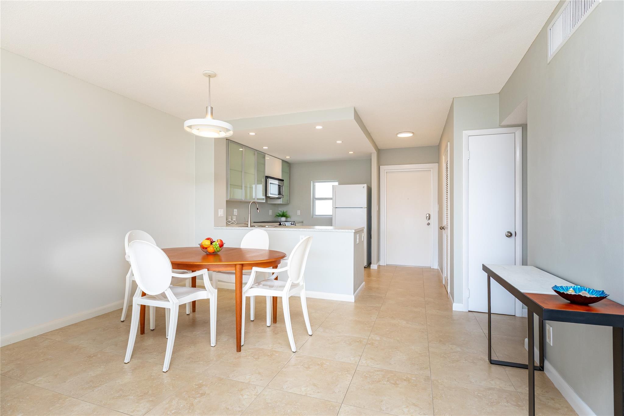 View from living into dining into kitchen with entry door in background. Hallway at right into guest bathroom and guest bedroom.