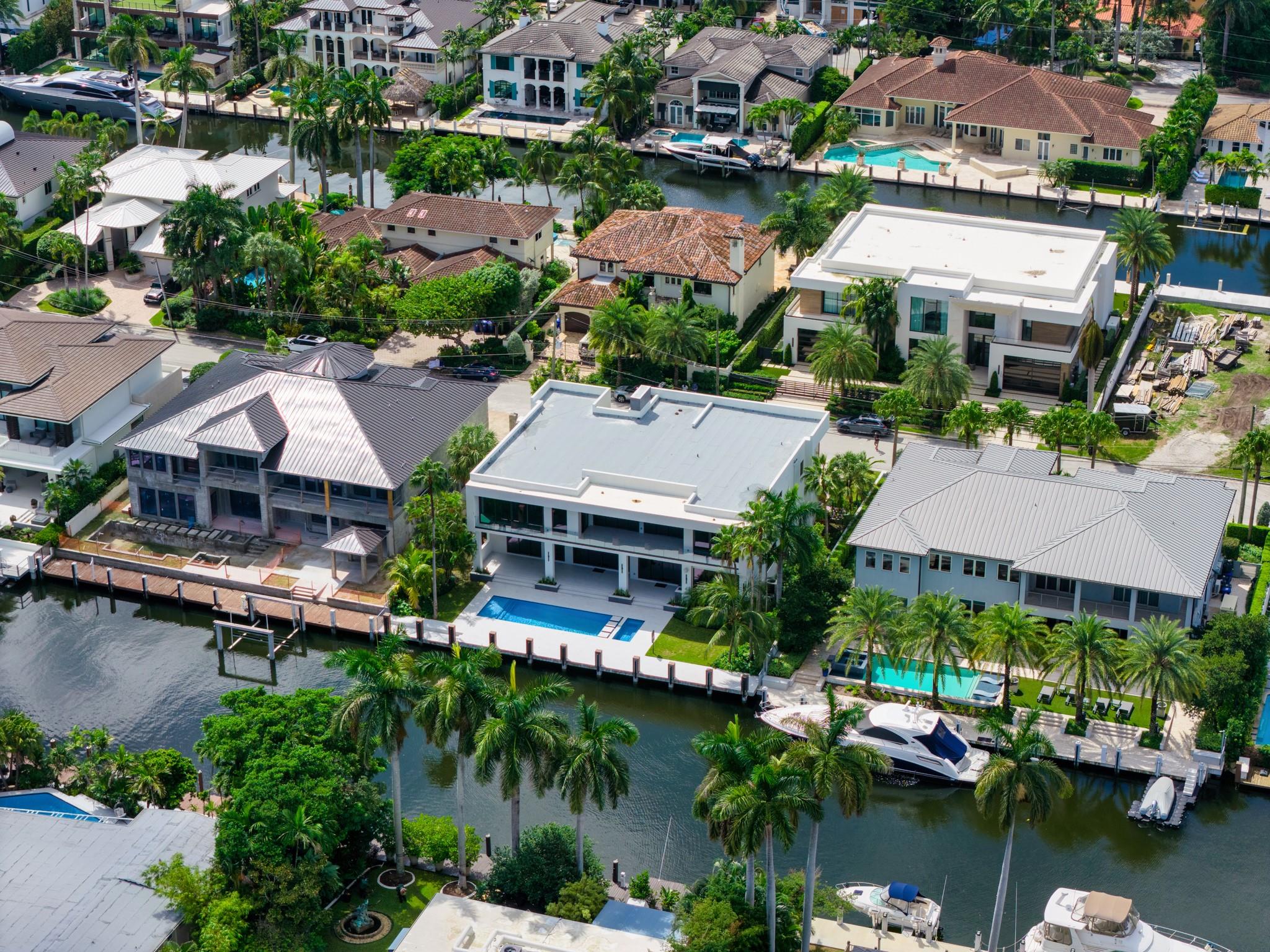 A direct overhead shot of a modern white residence with sleek architecture, set along the canal with tropical landscaping.
