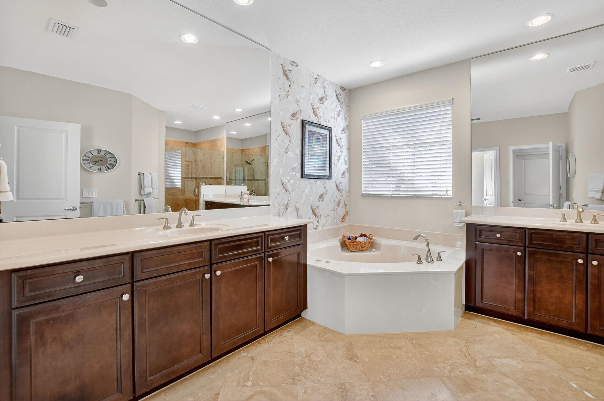 Light-filled primary bathroom with double vanities, whirlpool tub, and separate shower