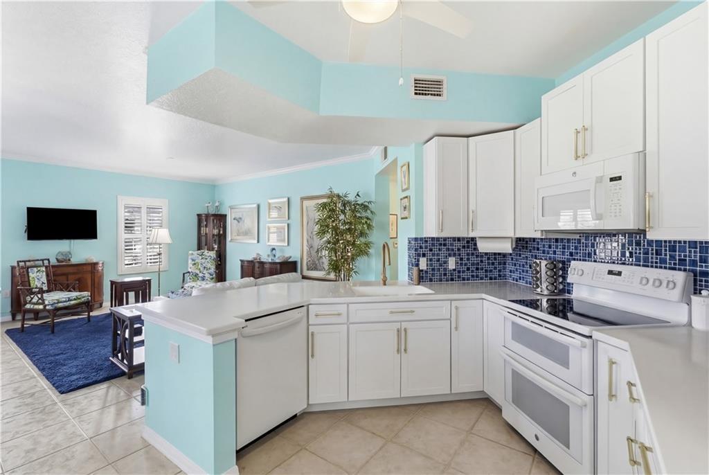 Kitchen featuring white appliances, open floor plan, white cabinets, light countertops, and ornamental molding