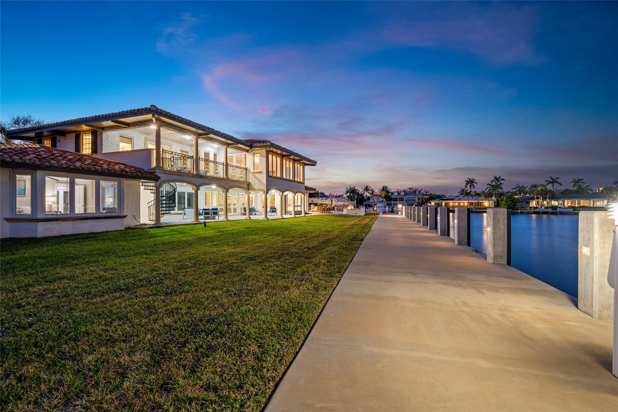 A breathtaking twilight waterfront elevation reflected in the shimmering pool, with expansive glass walls glowing against the evening sky. Dramatic and unforgettable, this estate embodies resort-caliber luxury in a spectacular coastal setting.