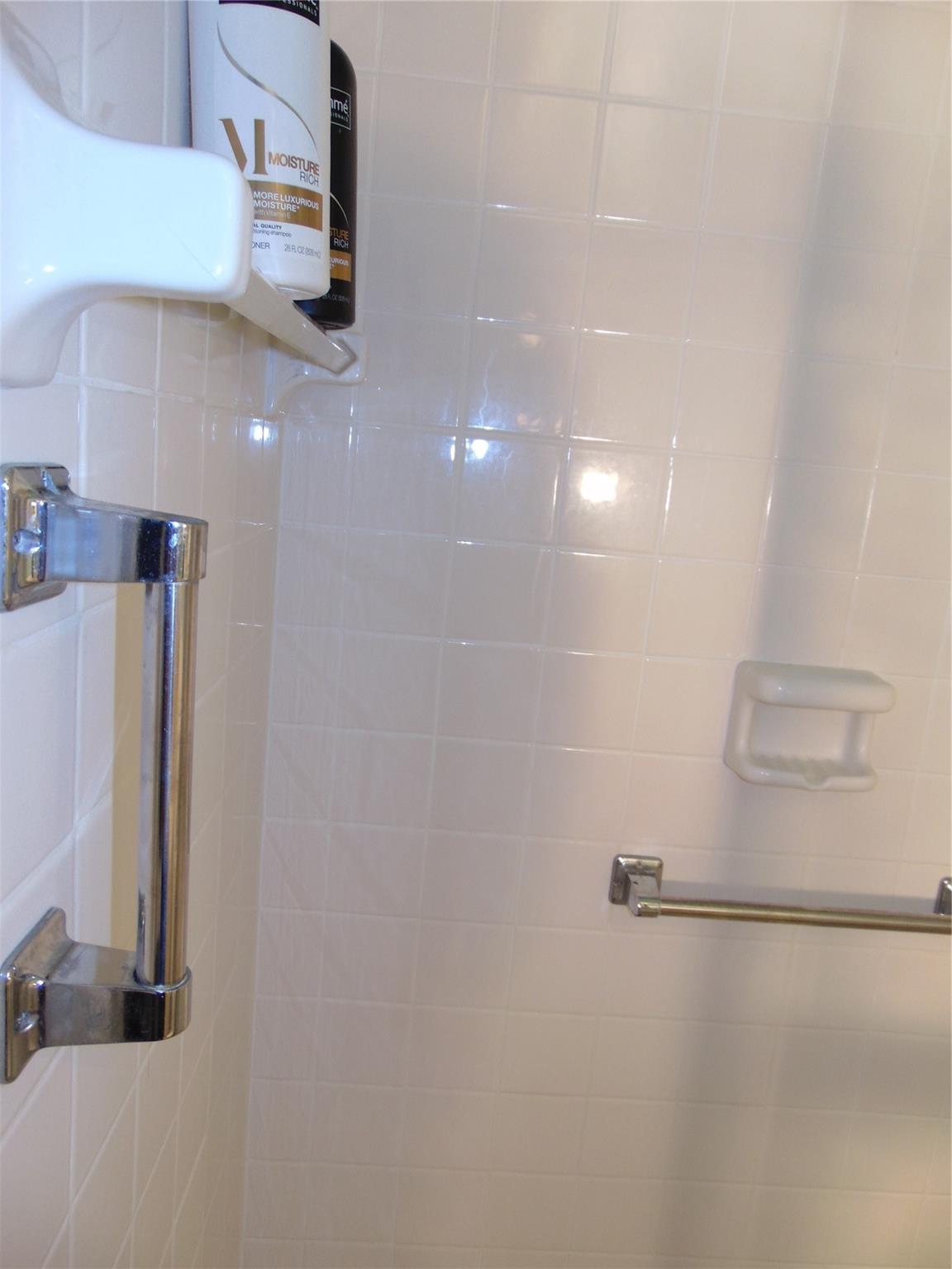 STALL SHOWER AT GUEST BATH WITH GRAB BARS AND ALL WHITE TILE.