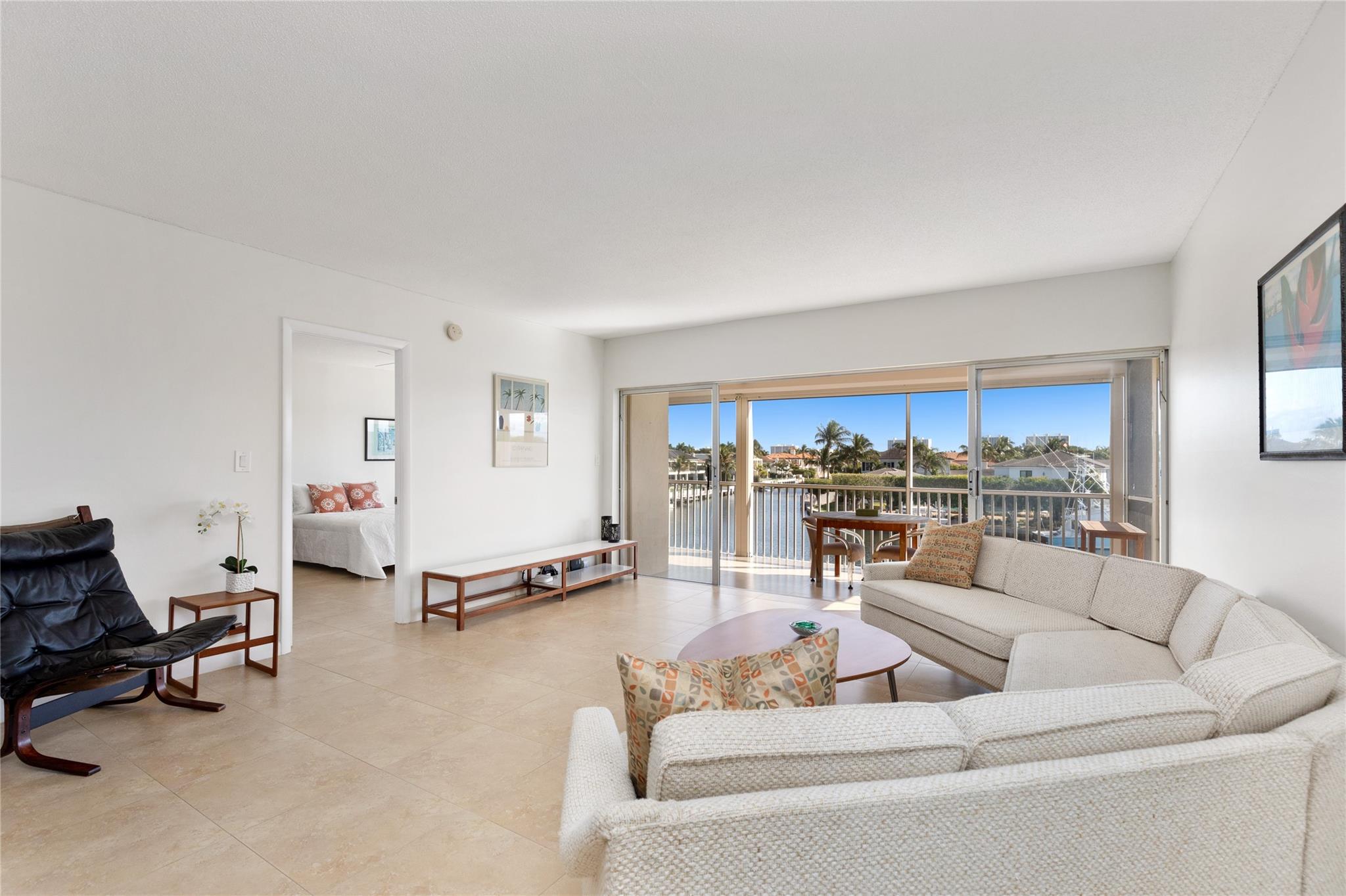 Living area with waterway in background off large balcony and primary bedroom in left background