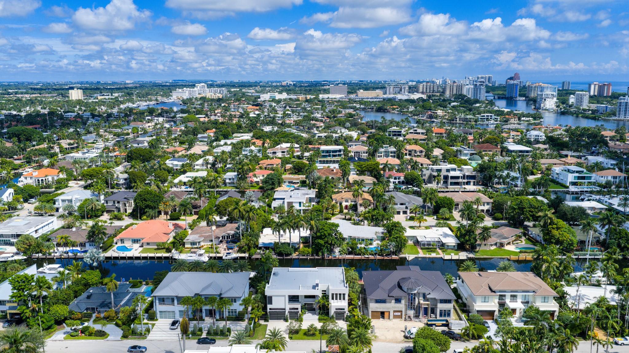 A vibrant neighborhood scene showing waterfront homes leading toward the Fort Lauderdale coastline and ocean horizon.