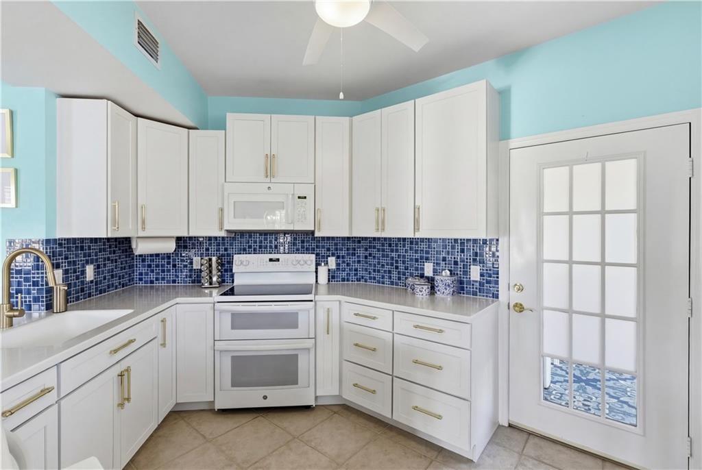 Kitchen with double overns, white cabinetry, light tile patterned floors, and light stone counters