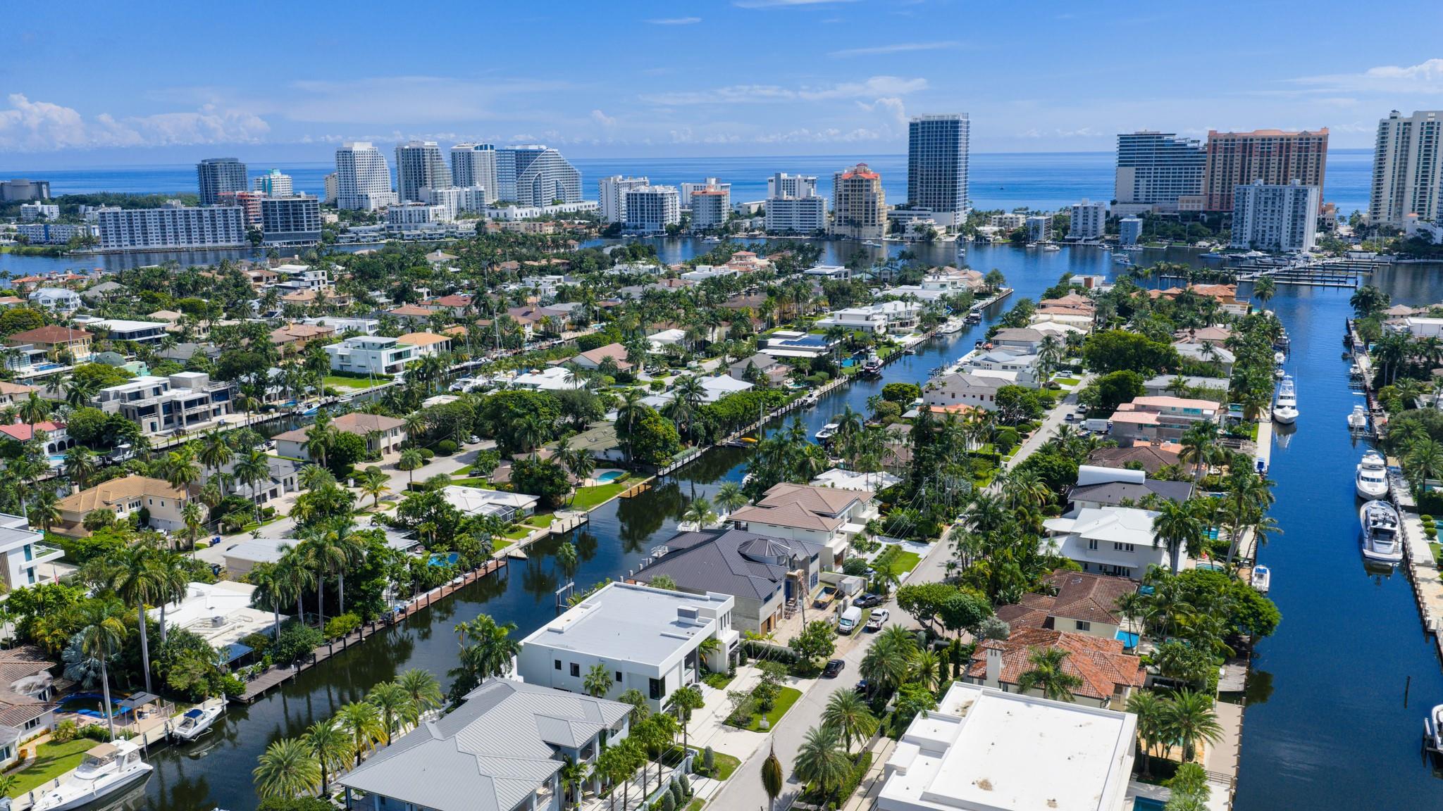 A vibrant neighborhood scene showing waterfront homes leading toward the Fort Lauderdale coastline and ocean horizon.