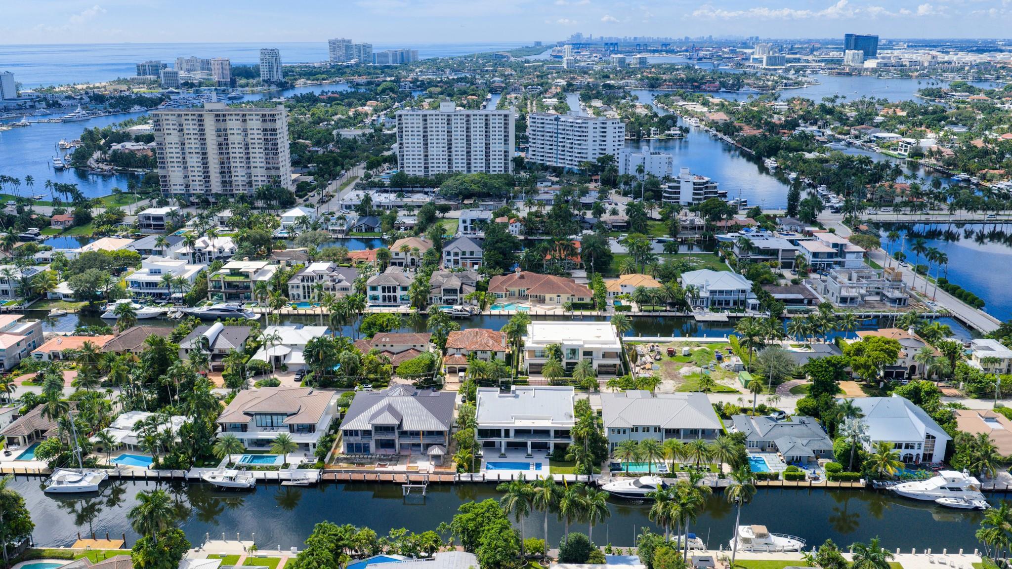 A vibrant neighborhood scene showing waterfront homes leading toward the Fort Lauderdale coastline and ocean horizon.