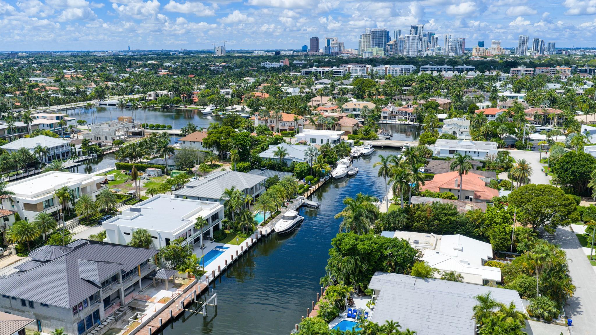 A sweeping aerial view of Fort Lauderdale’s luxury waterfront neighborhoods framed by canals, lush greenery, and the city skyline in the distance.