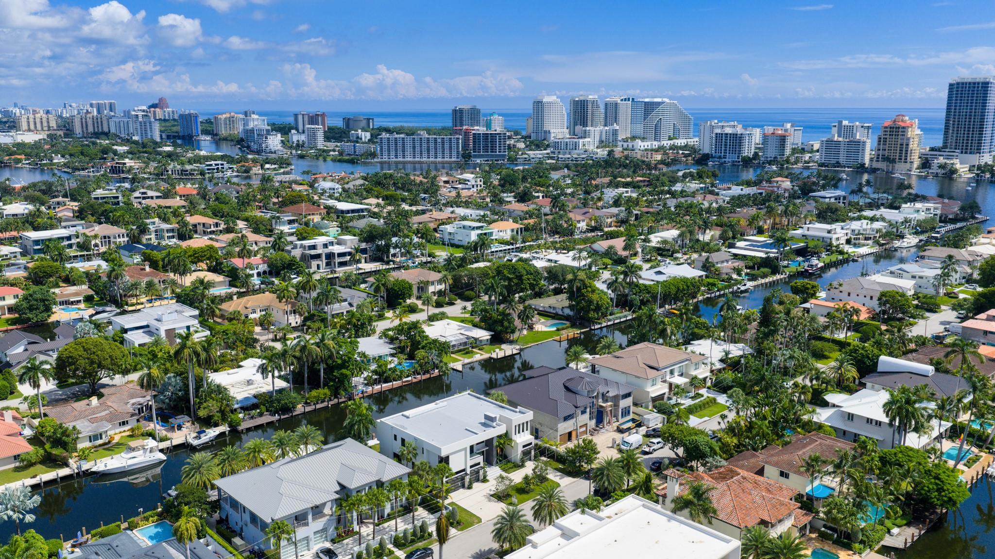 A vibrant neighborhood scene showing waterfront homes leading toward the Fort Lauderdale coastline and ocean horizon.