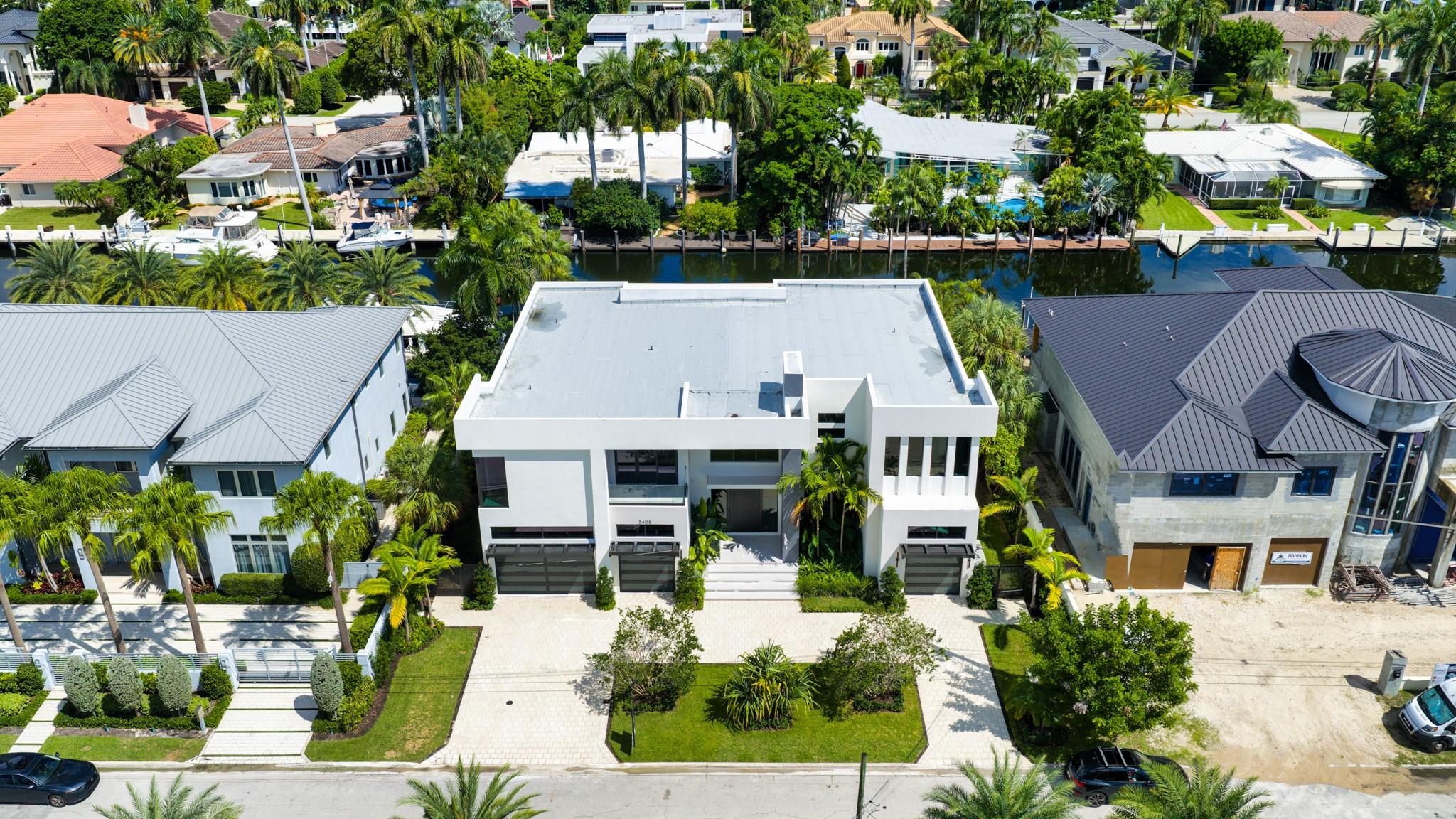 A direct overhead shot of a modern white residence with sleek architecture, set along the canal with tropical landscaping.