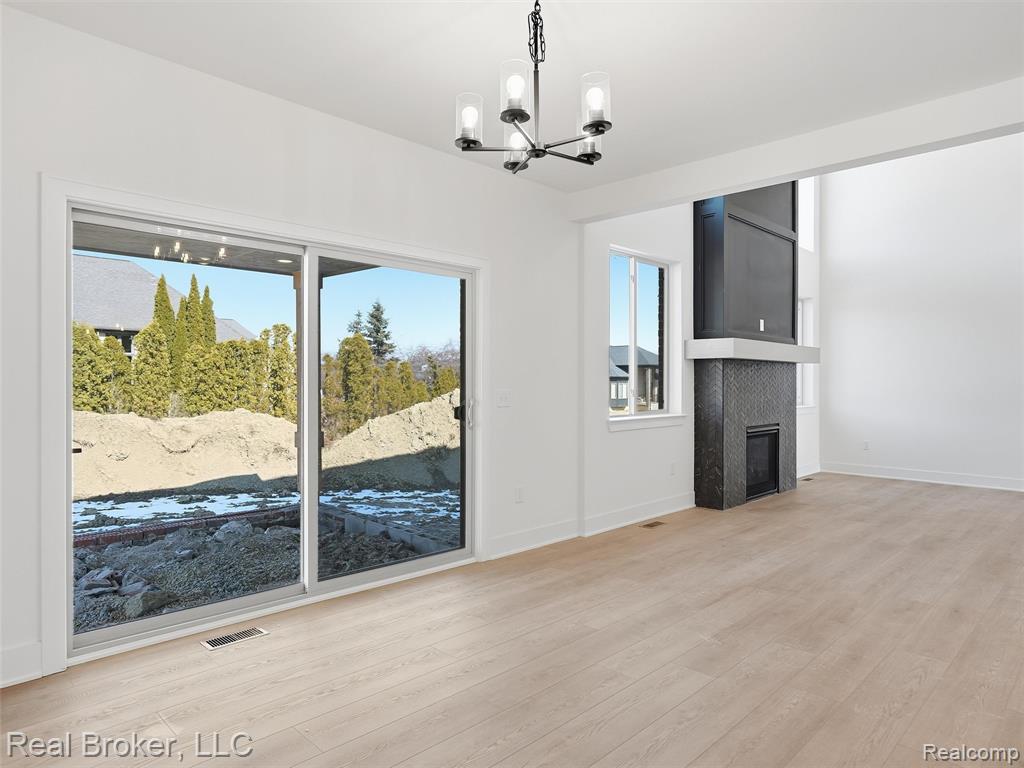 Unfurnished living room with light wood-type flooring, a chandelier, and a tiled fireplace