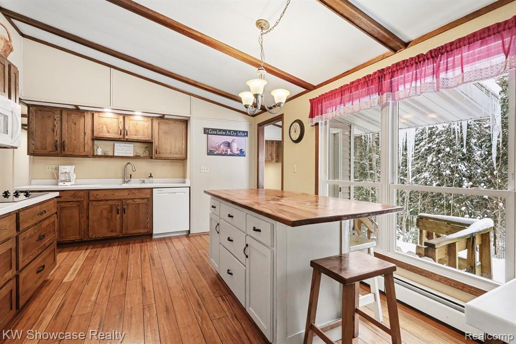 Dual tone kitchen with butcher block counters, dual tone cabinets, vaulted ceiling, hanging lights, and white appliances