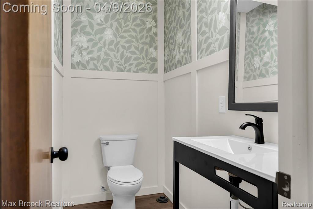 Bathroom with wallpapered walls, vanity, and dark wood-type flooring