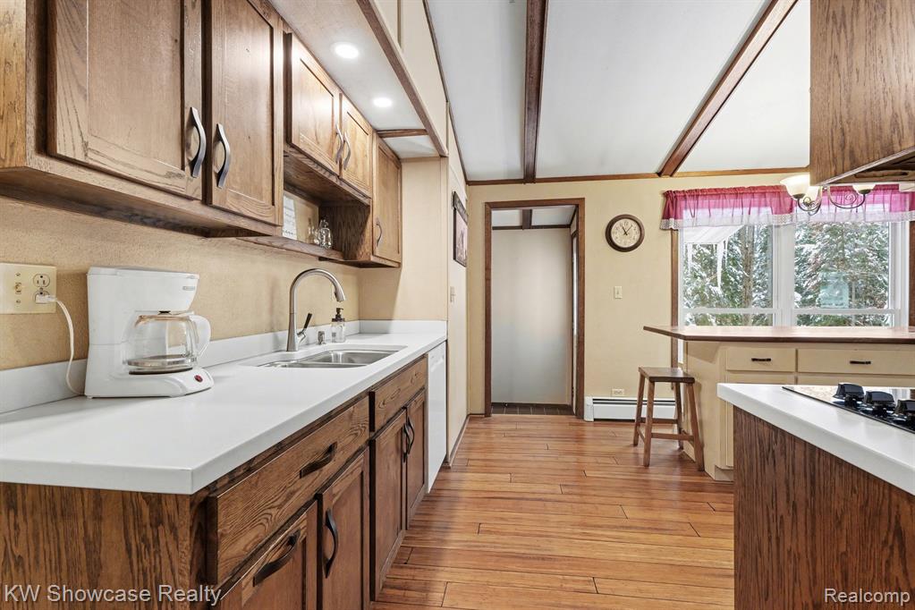 Kitchen with light wood finished floors, light countertops, beam ceiling, a baseboard heating unit, and dishwasher