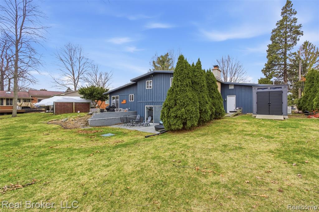 Rear view of property with a storage unit, a patio, a lawn, and a chimney
