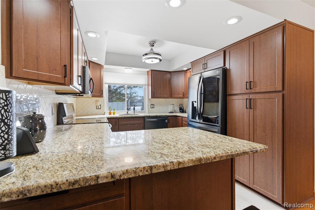 Kitchen with light stone counters, a peninsula, stainless steel appliances, wood finish cabinets, and recessed lighting