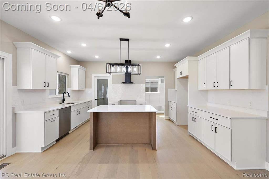 Kitchen featuring suspended lighting, white cabinetry, light wood-type flooring, and dishwasher