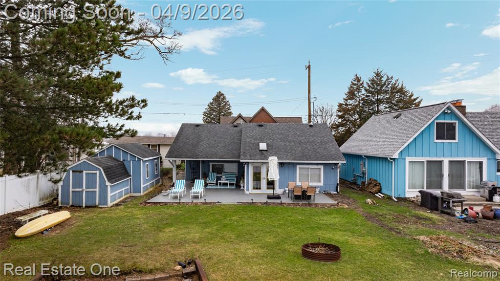 Rear view of property with a storage shed, a patio, an outdoor fire pit, a shingled roof, and board and batten siding