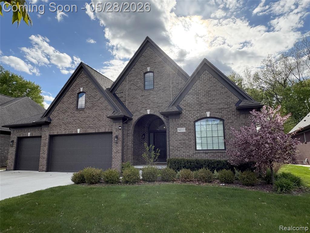 View of front of home with brick siding, a front yard, and concrete driveway