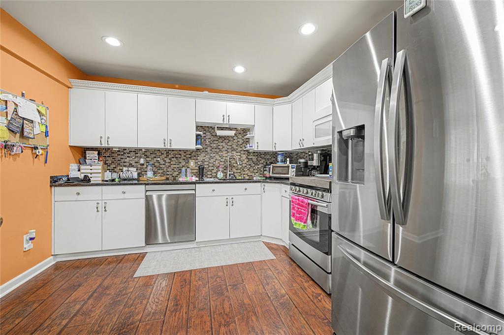 Kitchen with stainless steel appliances, white cabinetry, dark wood-style floors, tasteful backsplash, and recessed lighting