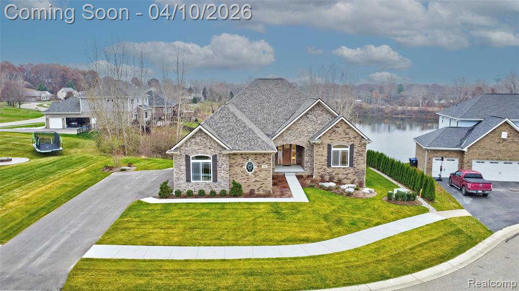 View of front of property with a front yard, a water view, stone siding, and brick siding