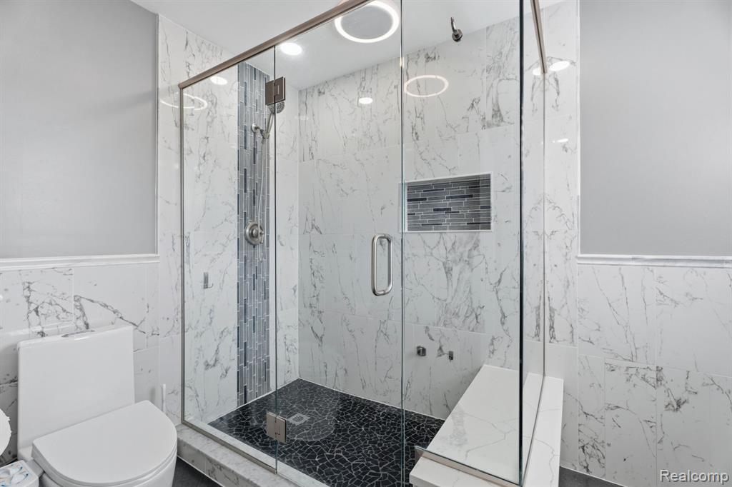 Full bathroom with tile walls, a wainscoted wall, and a marble finish shower