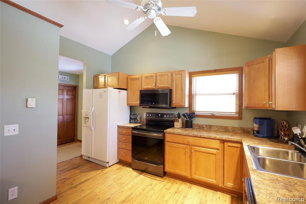 Kitchen with black range with electric cooktop, ceiling fan, stainless steel microwave, white refrigerator with ice dispenser, and light countertops
