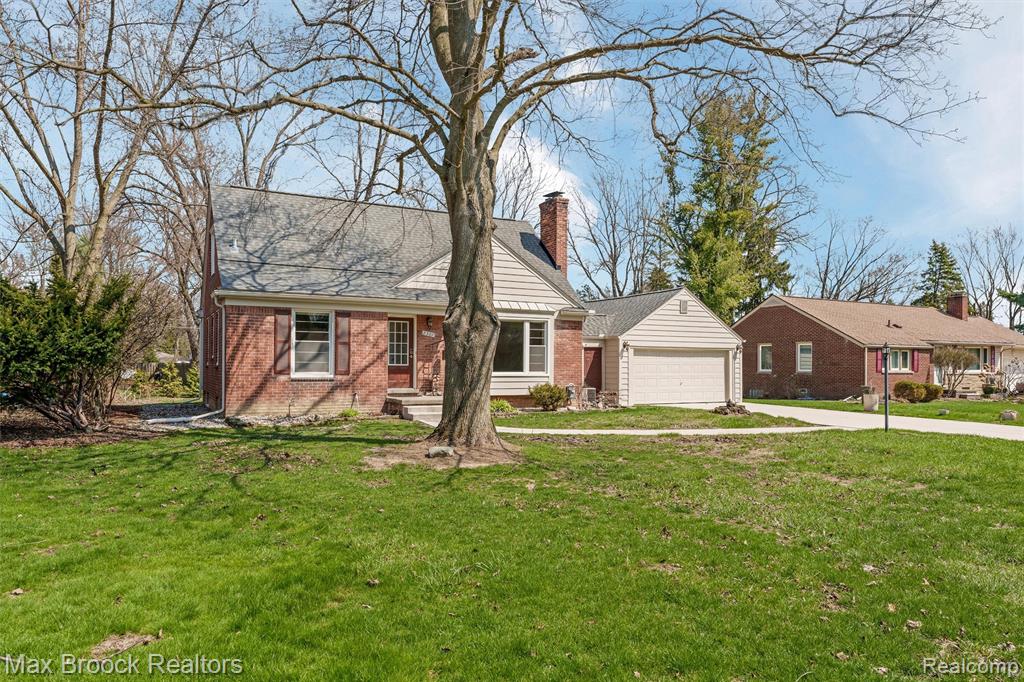 View of front facade with a chimney, brick siding, a front lawn, and concrete driveway