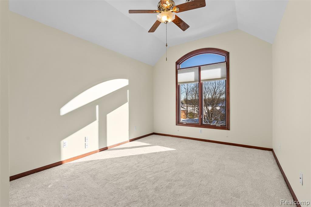 Carpeted spare room featuring ceiling fan and vaulted ceiling