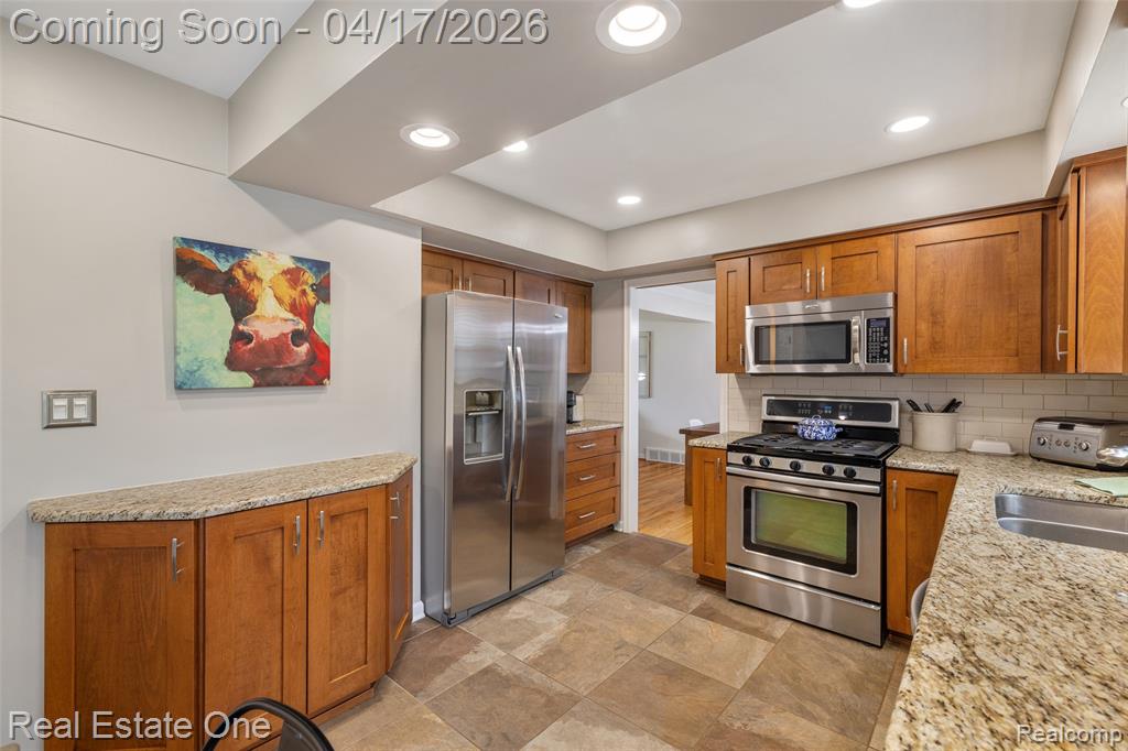 Kitchen featuring wood finish cabinetry, stainless steel appliances, light stone countertops, backsplash, and recessed lighting