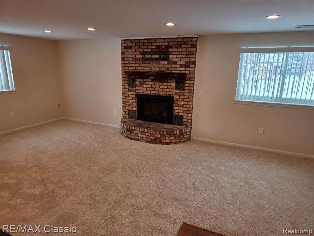 Unfurnished living room with a brick fireplace, recessed lighting, and carpet floors