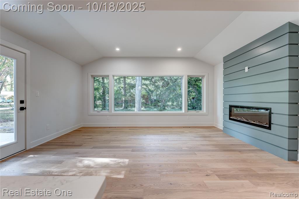 Unfurnished living room with a glass covered fireplace, light wood-type flooring, vaulted ceiling, healthy amount of natural light, and recessed lighting