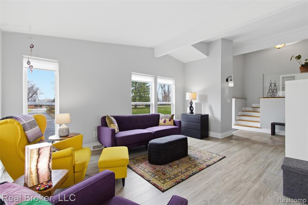 Living area with light wood-style floors, healthy amount of natural light, and lofted ceiling with beams