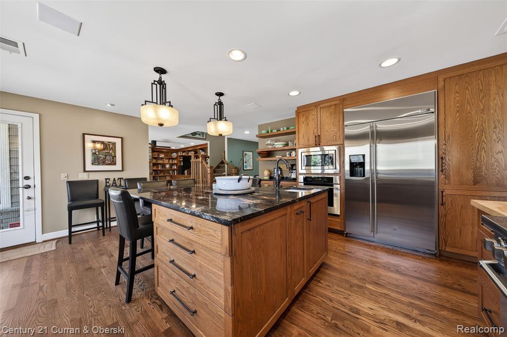 Kitchen with wood finish cabinets, open shelves, built in appliances, a center island with sink, and hanging light fixtures