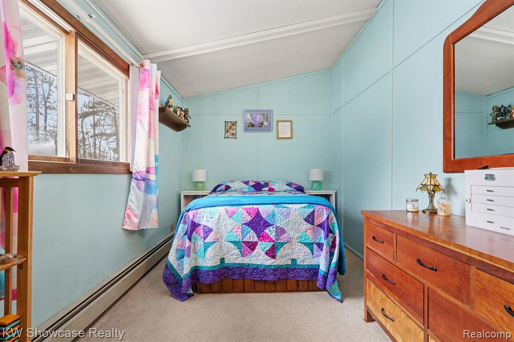 Bedroom with a baseboard heating unit, vaulted ceiling, and light colored carpet