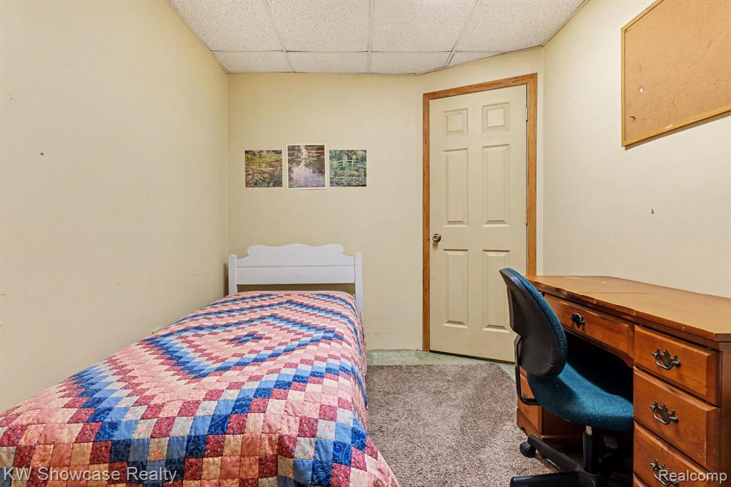 Bedroom with a drop ceiling, a desk, and light carpet