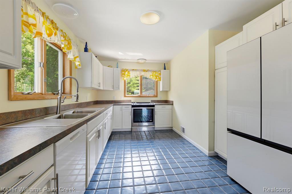 White cabinetry, stainless steel sink, integrated dishwasher, full-size refrigerator, and tile flooring