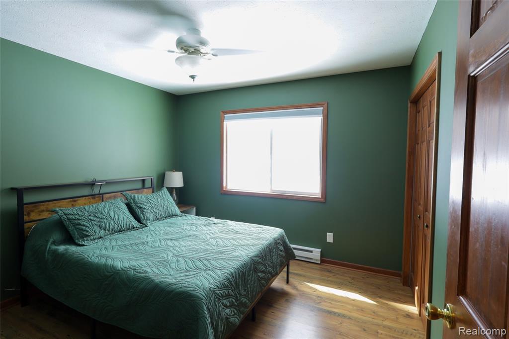 Bedroom with wood finished floors, a baseboard heating unit, and ceiling fan