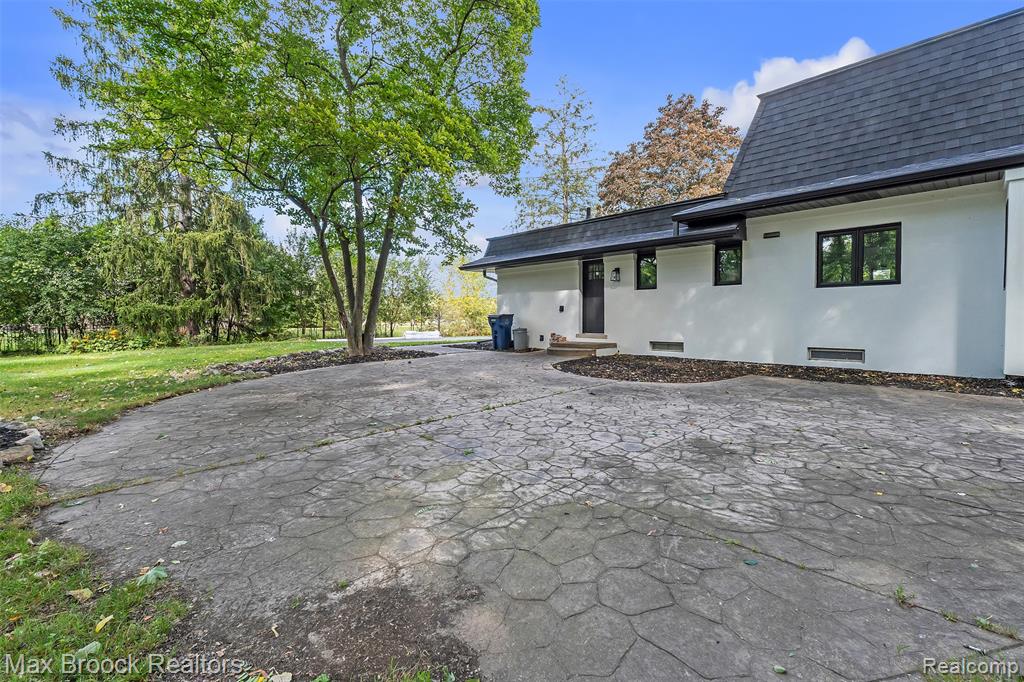 Rear view of house with stucco siding, roof with shingles, a patio area, a lawn, and driveway