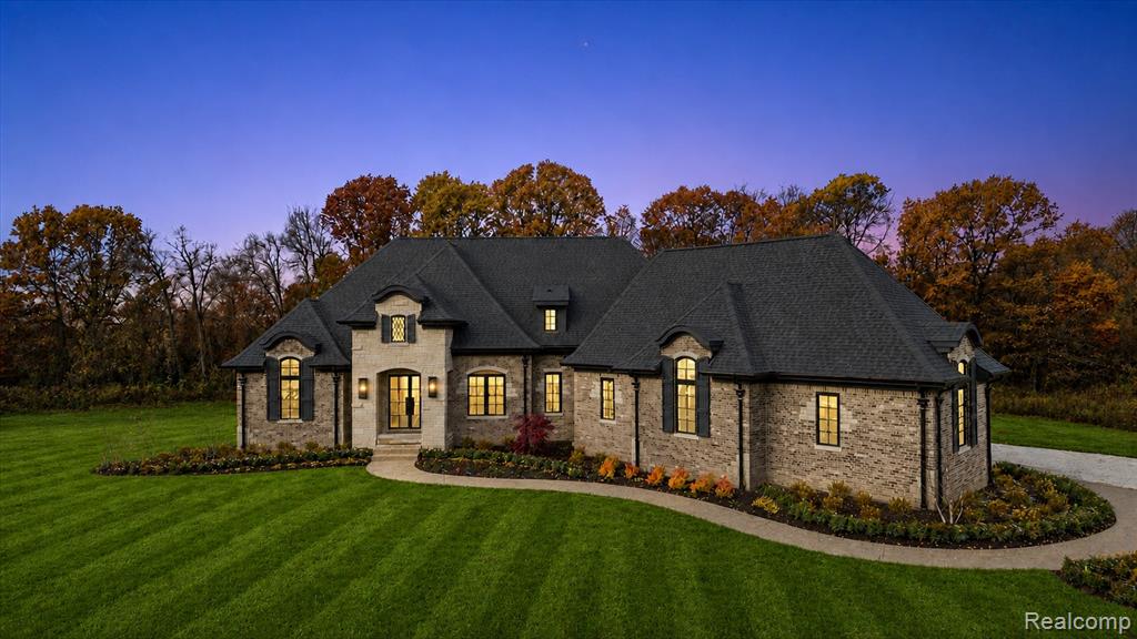 Stately stone and brick residence featuring a multi-gabled roofline, arched window dormers, and a paved circular driveway