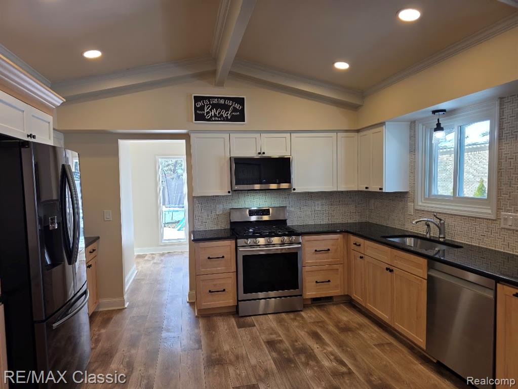 Kitchen with appliances with stainless steel finishes, crown molding, dark wood-style floors, dark stone countertops, and plenty of natural light