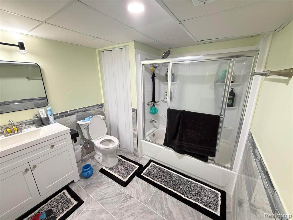 Bathroom featuring a wainscoted wall, enclosed tub / shower combo, vanity, tile walls, and light marble finish flooring