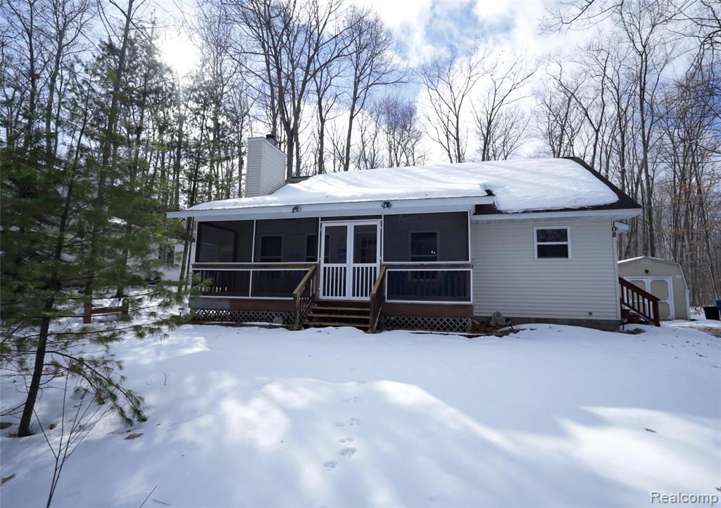 View of front of home with a sunroom, a chimney, and a storage unit