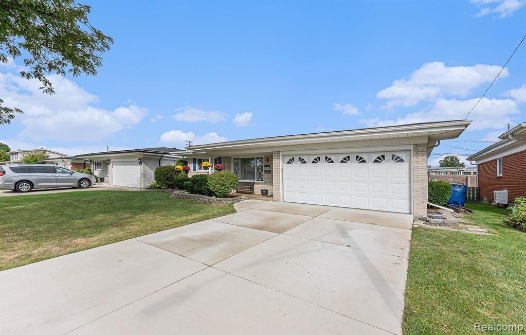 Ranch-style home with brick siding, a front lawn, an attached garage, and driveway