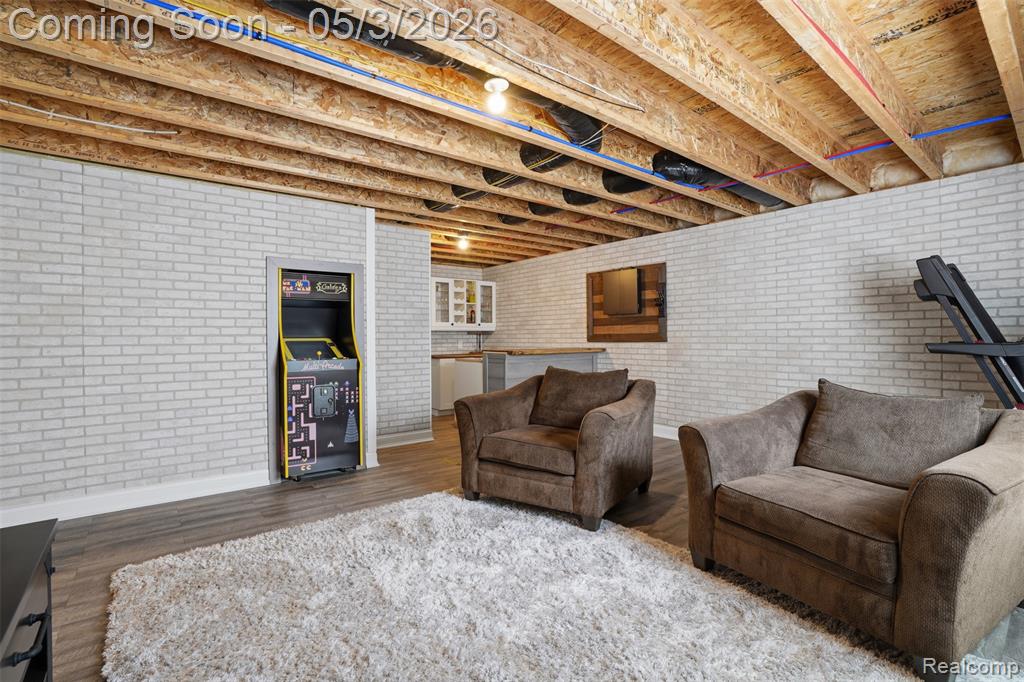Finished lower level room featuring wood finished floors and brick wall